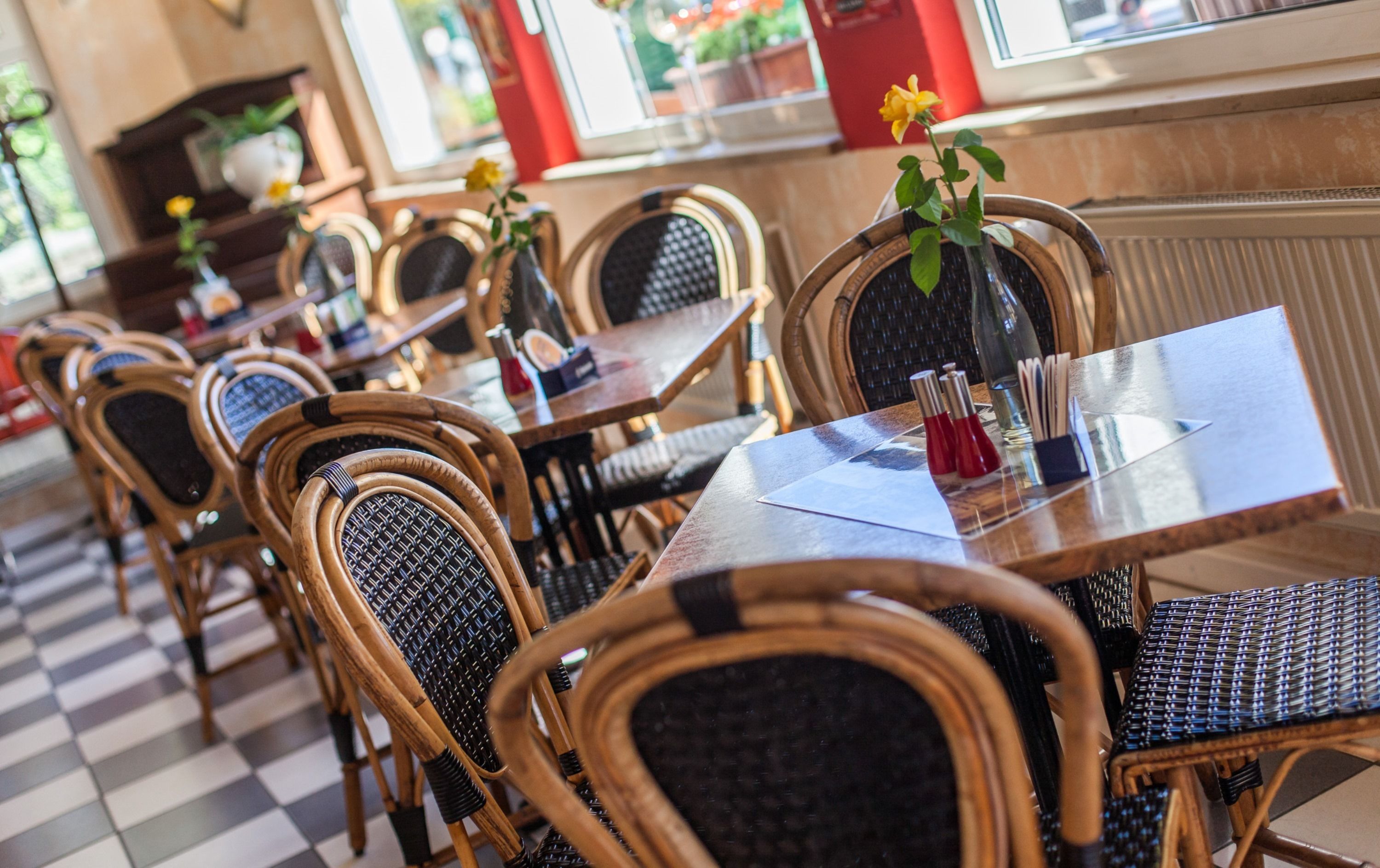 A restaurant with wicker chairs and tables, some with flowers.