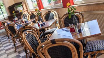 A restaurant with wicker chairs and tables, some with flowers.