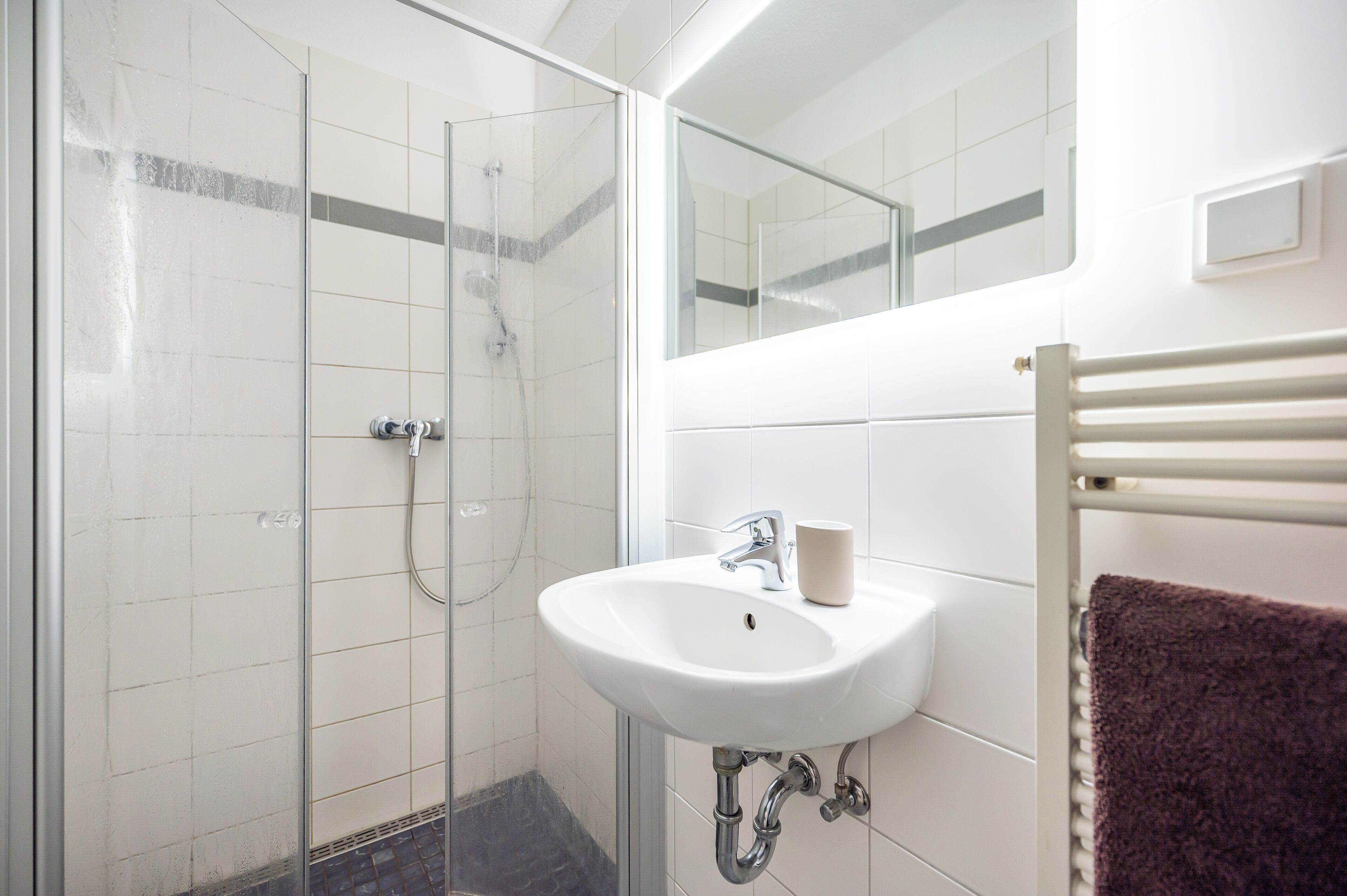 A bathroom with a glass shower enclosure, a white sink, and a towel rack.