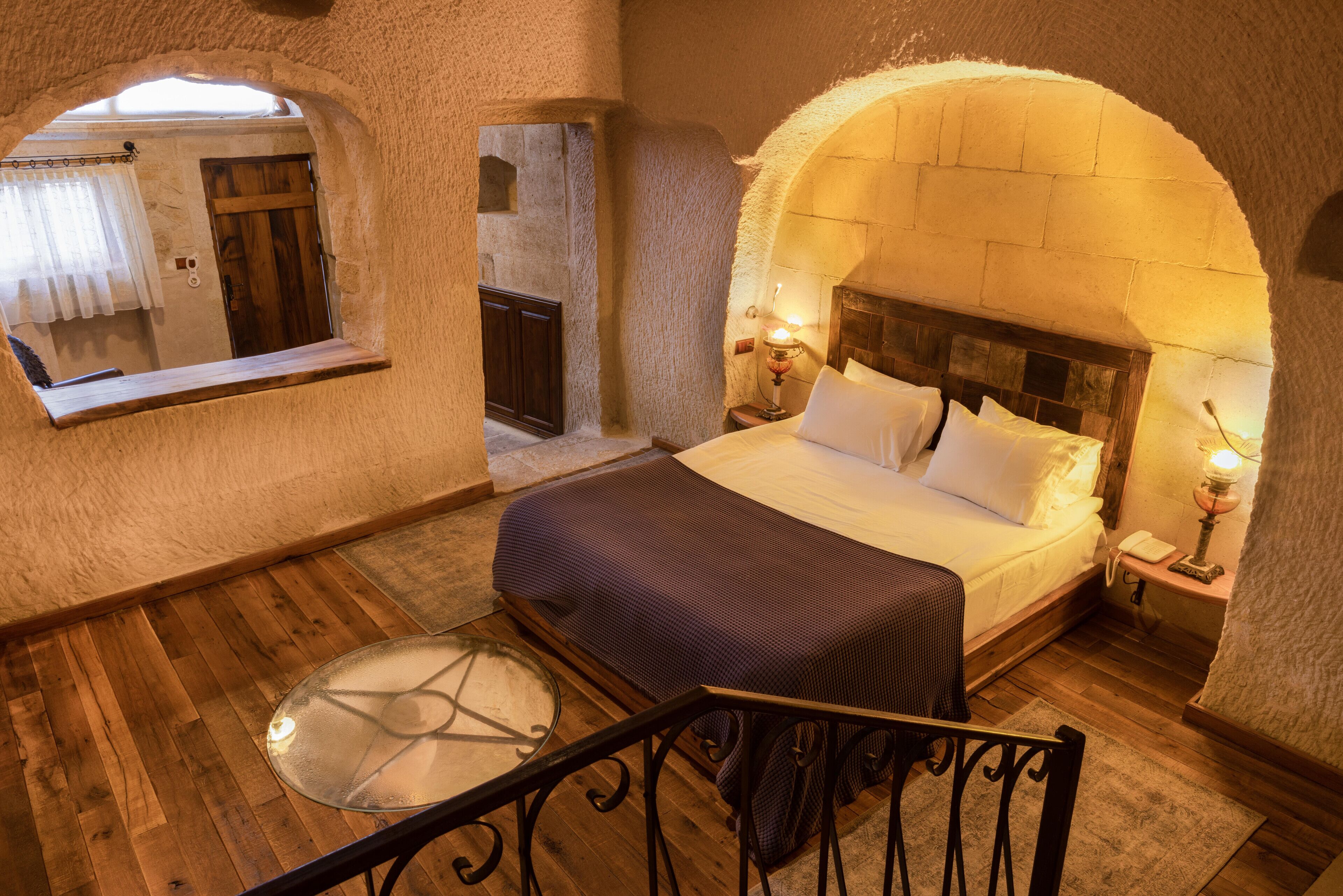 Ein Schlafzimmer mit Holzboden, einem Bett mit weißen Leinen, einem Nachttisch mit Lampe und einem kleinen, runden Fenster.