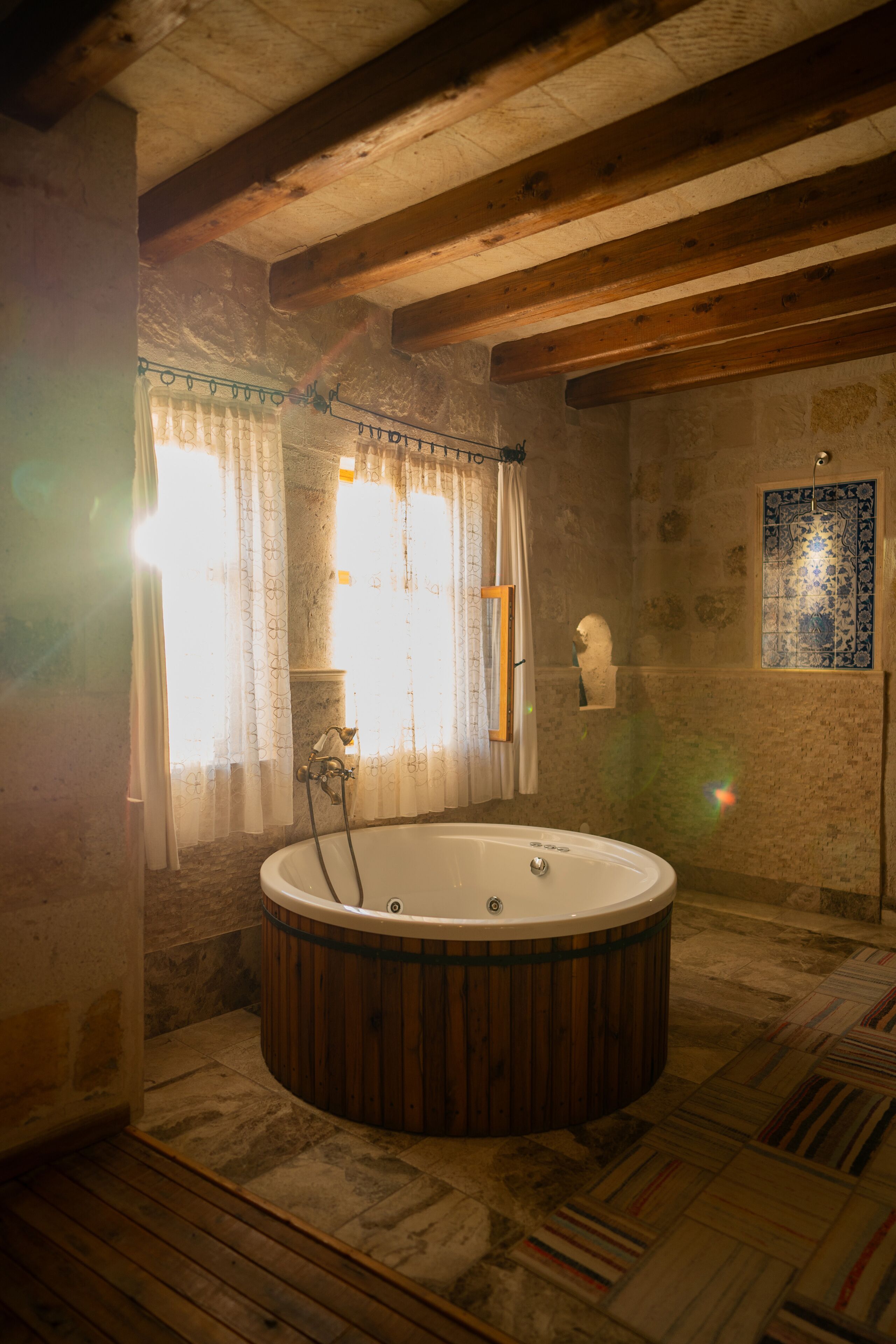 A rustic bathroom with a wooden bathtub, stone walls, and a tiled floor.