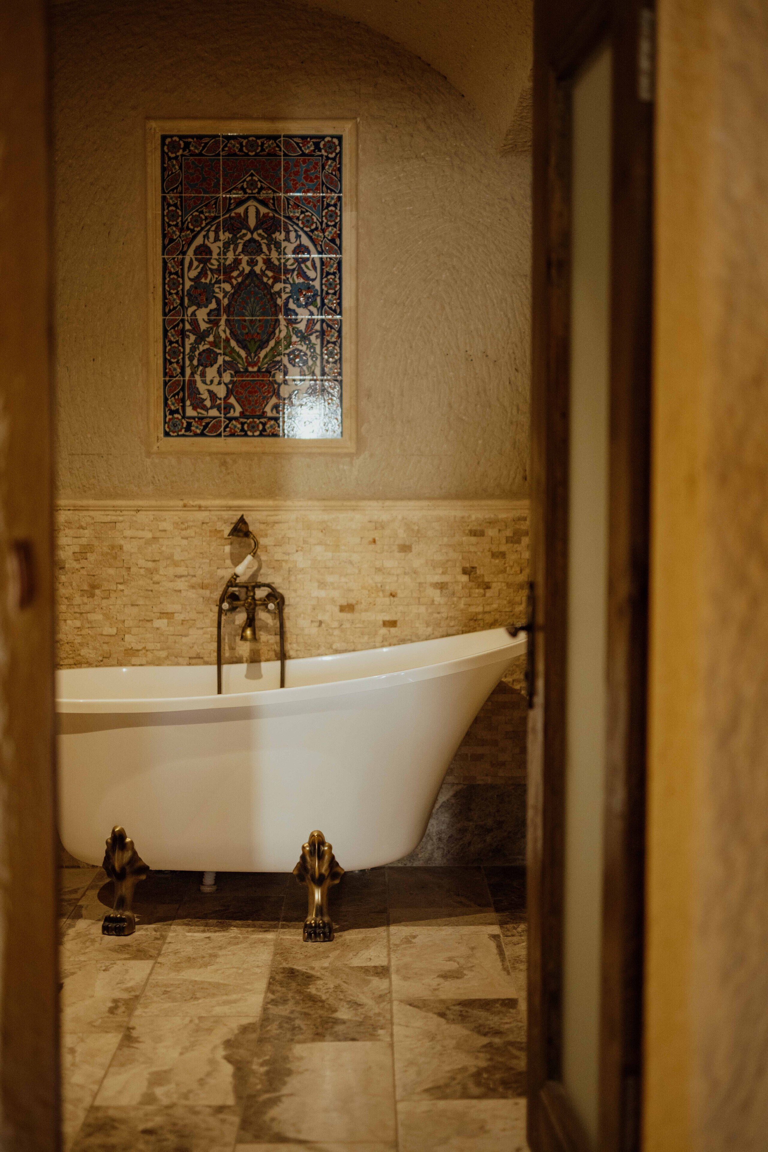 A bathroom with a freestanding bathtub, a mosaic tile wall, and a tiled floor.