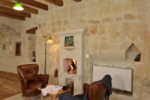 A cozy room with a stone fireplace, a leather armchair, a table with a cup and saucer, and a radiator.