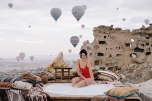 A person sitting on a bed with a view of hot air balloons and a rocky landscape.