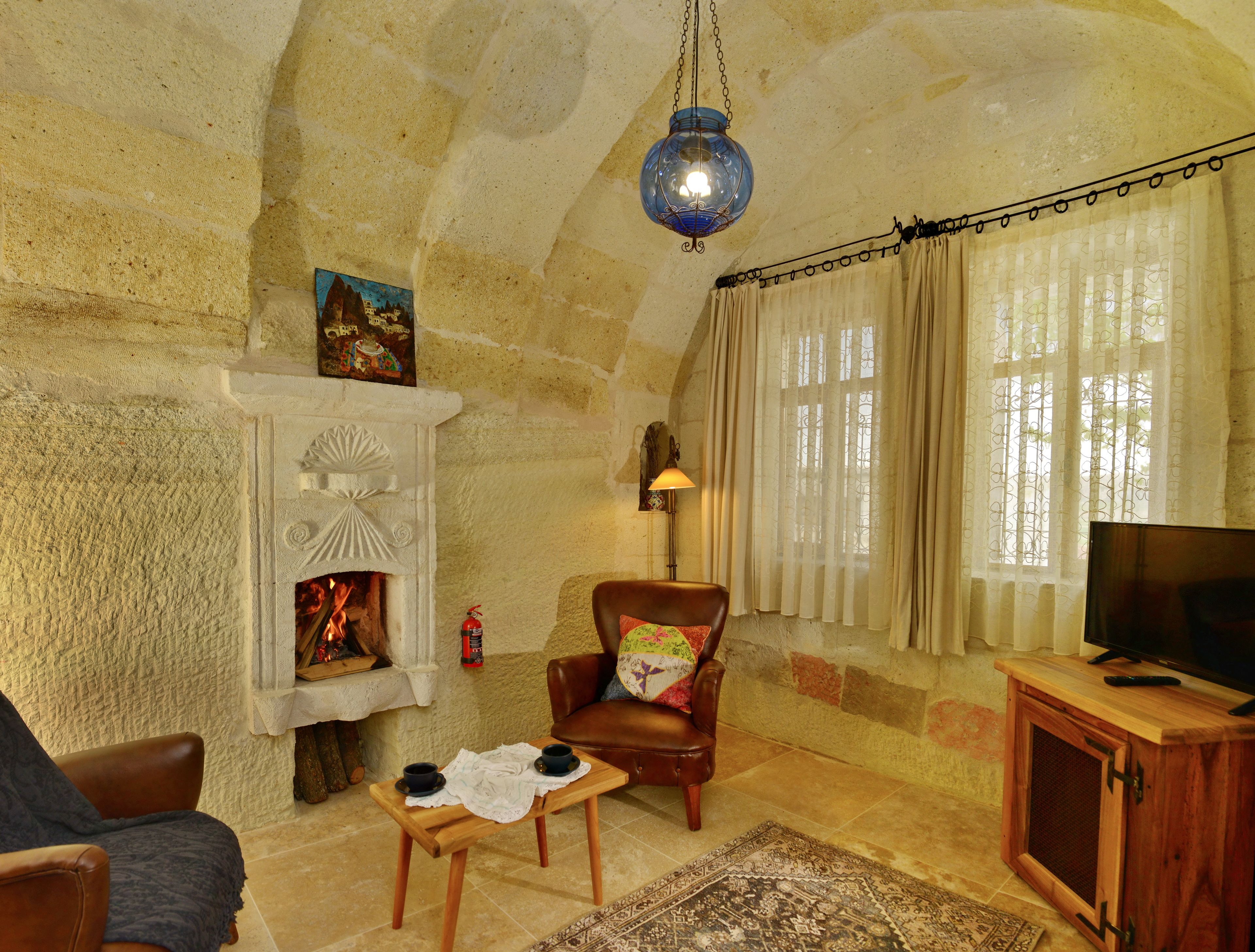 A cozy living room with a fireplace, a leather armchair, a wooden coffee table, and a television on a wooden cabinet.
