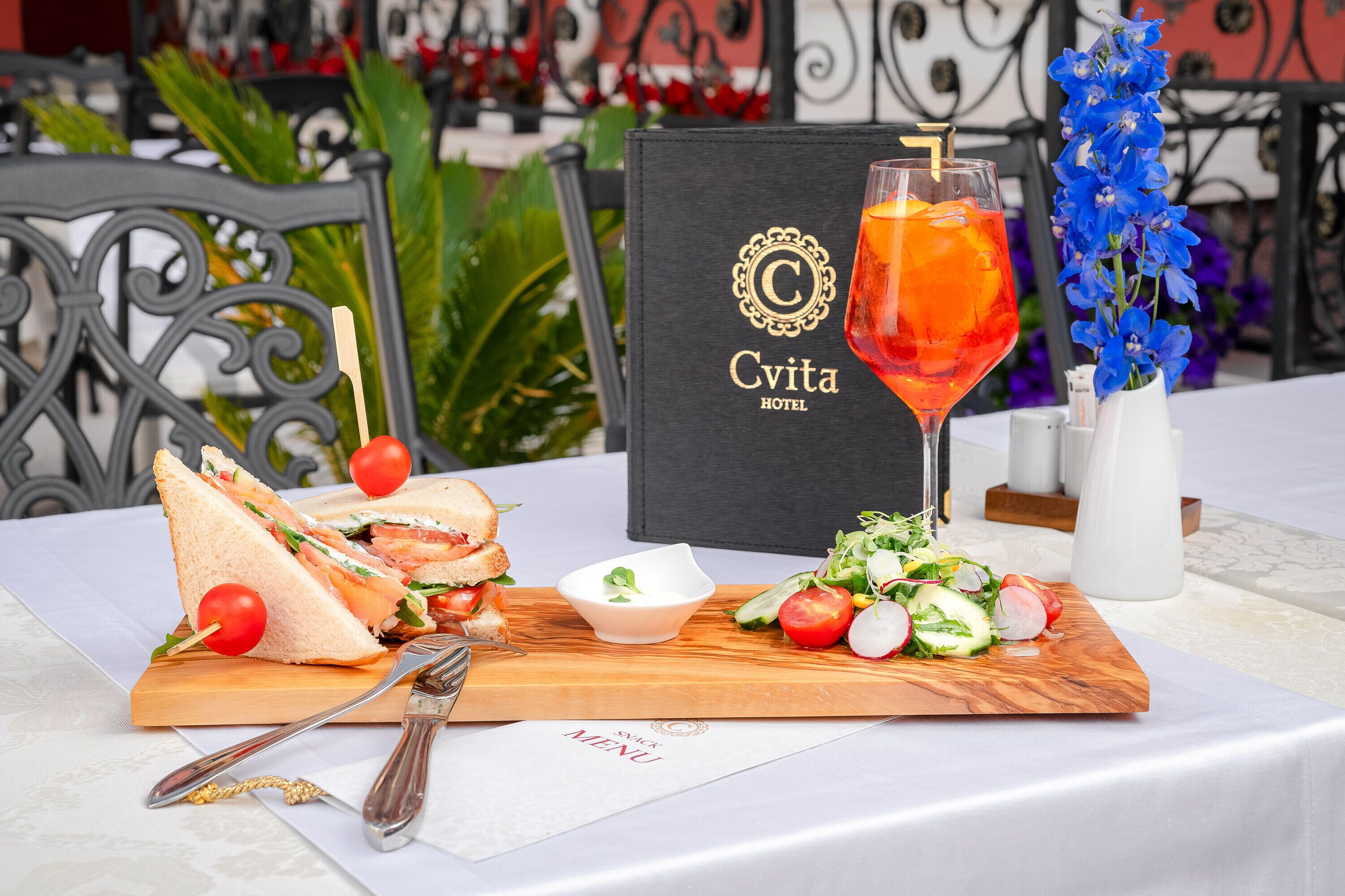 A table with a sandwich, a drink, a salad, and a menu at the Cvita Hotel.