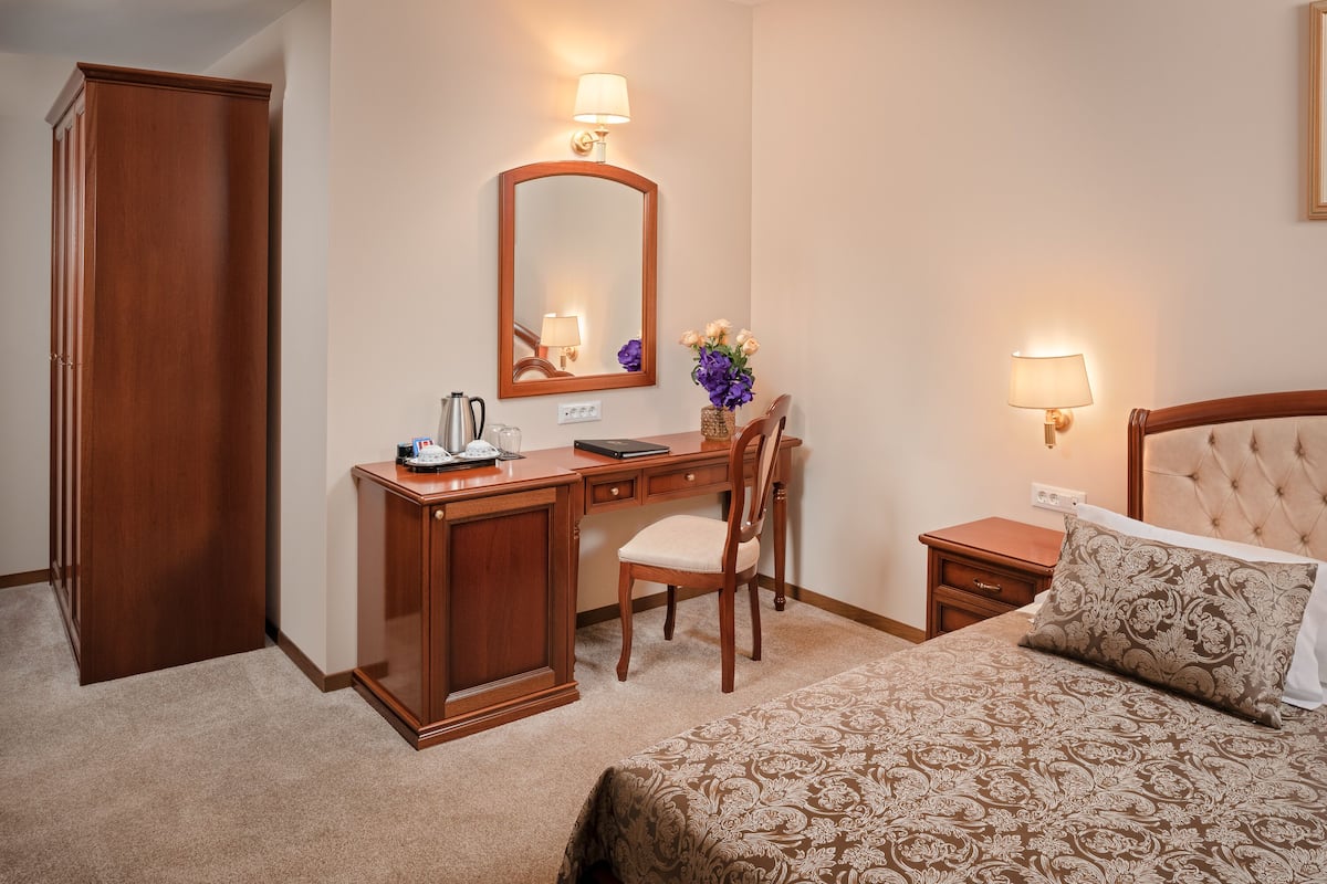 A hotel room with a bed, a desk with a chair, a wardrobe, a bedside table, and a nightstand.
