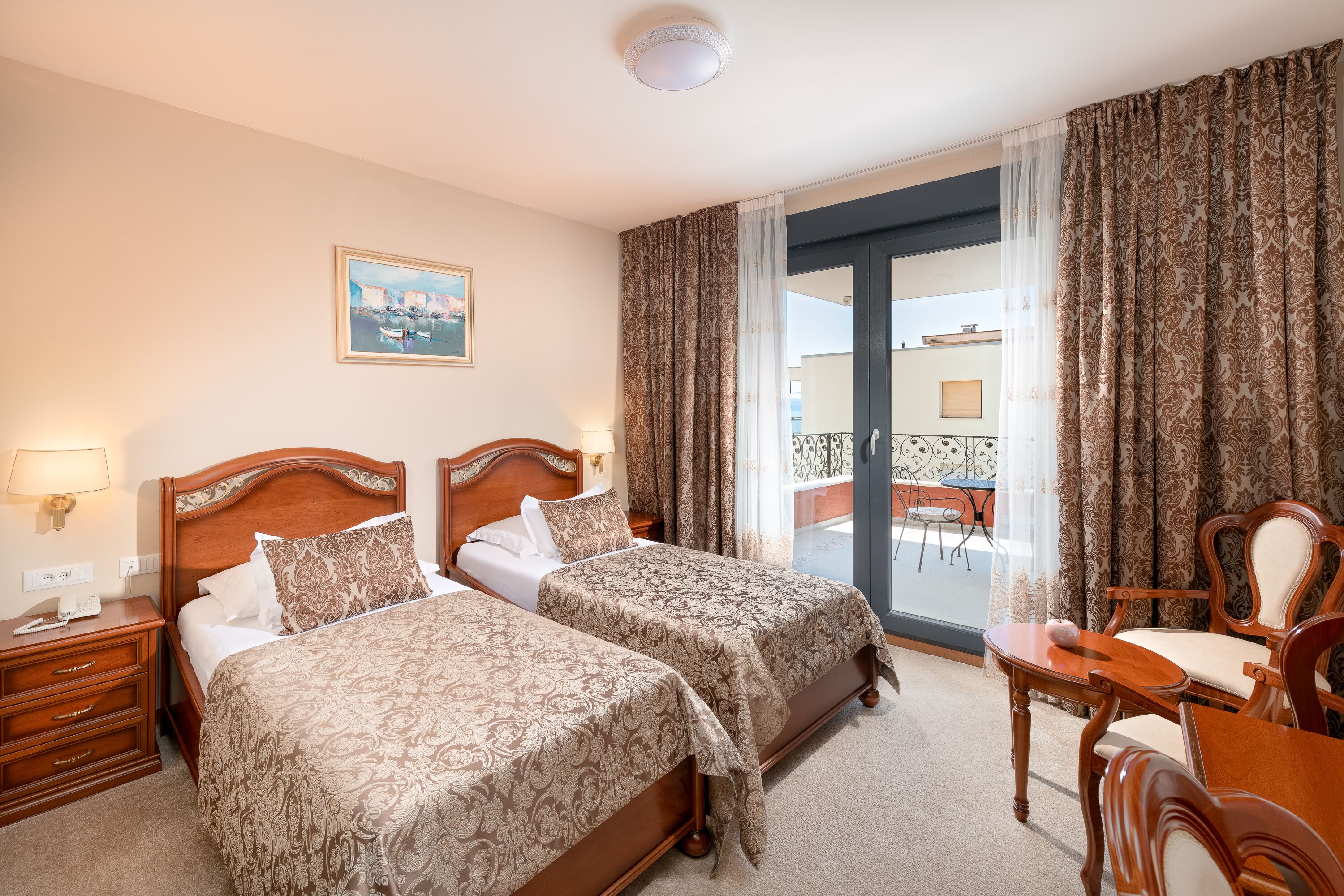 Une chambre d’hôtel avec deux lits, une tête de lit en bois, un tableau au mur et un balcon avec une table et des chaises.