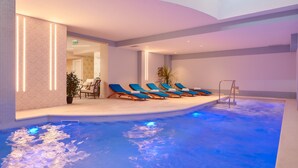Une piscine intérieure moderne, dotée d’un éclairage bleu, de chaises longues et d’un espace détente avec une table et des chaises.