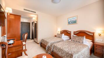 Une chambre d’hôtel avec deux lits, un bureau avec une chaise, une petite table et une lampe fixée au mur.