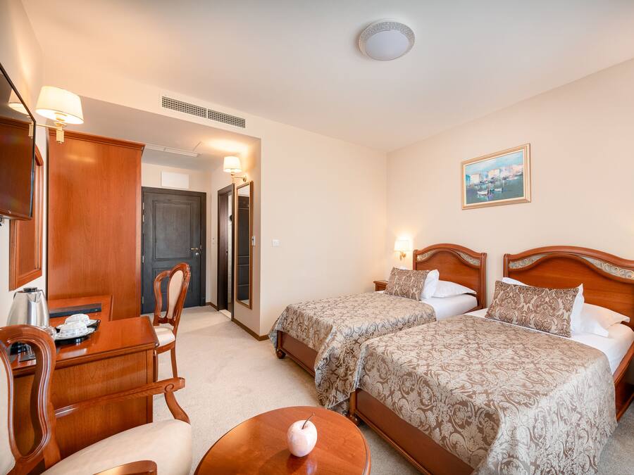 Une chambre d’hôtel avec deux lits, un bureau avec une chaise, une petite table et une lampe fixée au mur.