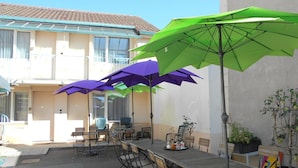 Une terrasse extérieure avec une longue table en bois et plusieurs chaises, entourée de parasols verts et violets.