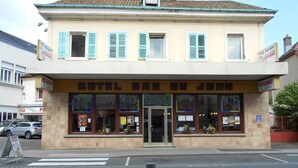 Un hôtel appelé « HOTEL BRU DU JUNE », avec une façade jaune, des volets bleus et une devanture ornée d’une enseigne de café.