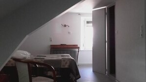 Une chambre avec un plafond en pente, un lit, une chaise et un radiateur.