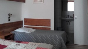 Une chambre avec deux lits, une tête de lit en bois, une table de chevet et un tableau encadré au mur. On aperçoit également la salle de bain à travers une porte ouverte.
