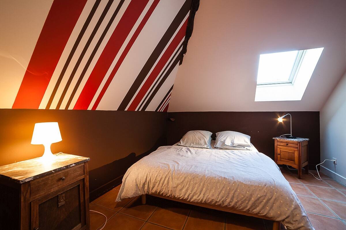 Een slaapkamer met een bed, een nachtkastje, een lamp en een dakraam.