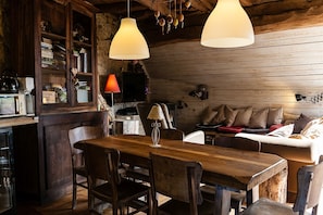 A rustic wooden interior with a wooden dining table, chairs, a sofa, and hanging lamps.