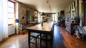 Une cuisine spacieuse avec une longue table en bois, des luminaires suspendus et un mur en pierre rustique.