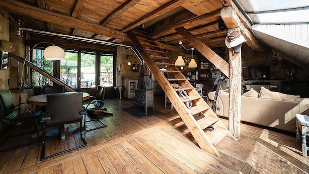 Un intérieur rustique avec un escalier en bois, un coin repas comprenant des chaises et une table, et un espace de vie chaleureux avec un canapé.