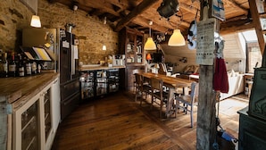 Une cuisine rustique avec des poutres en bois, un mur en pierre et une table à manger en bois, accompagnée de chaises.