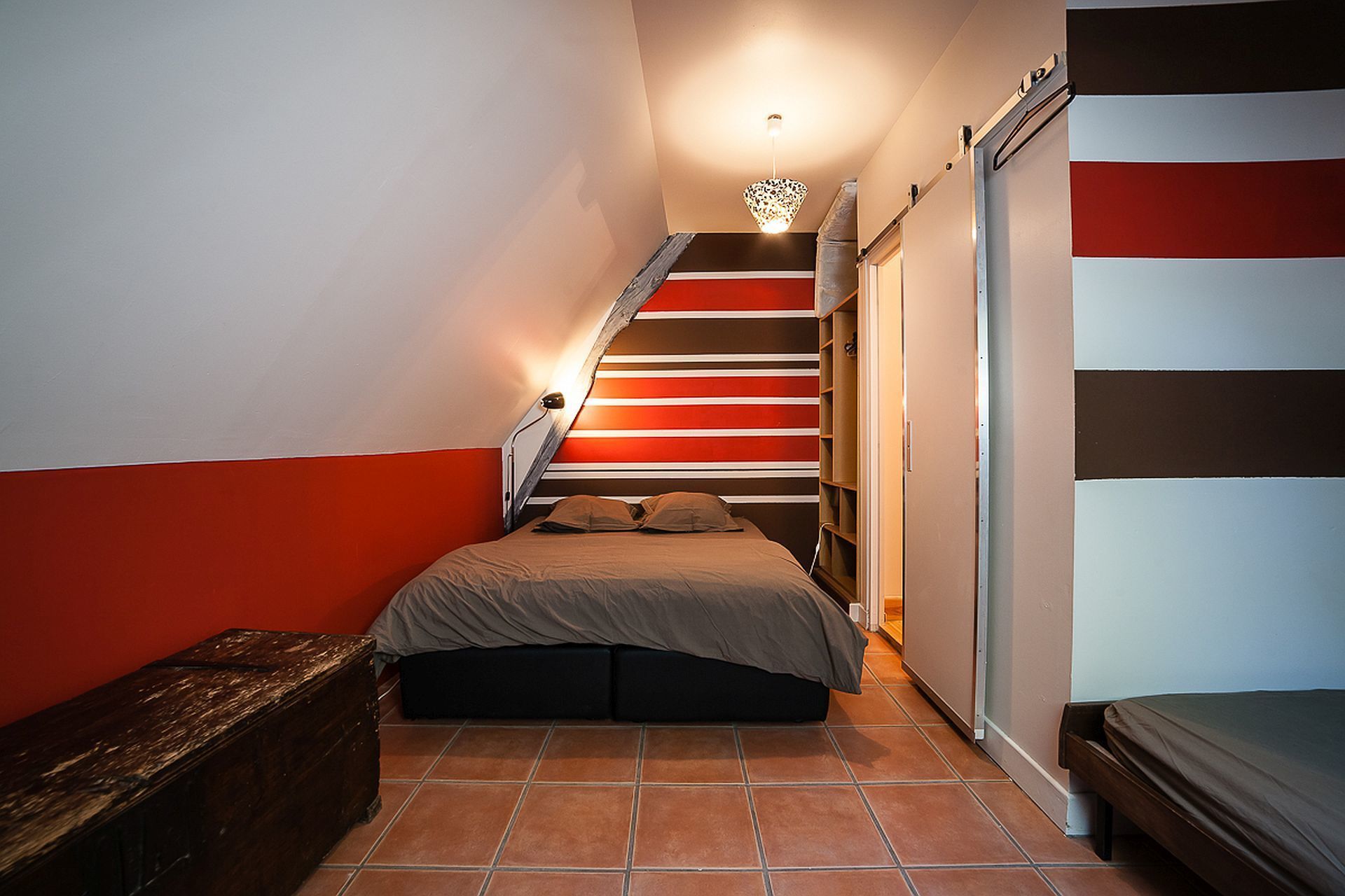 A narrow room with a bed, a wooden bench, and a staircase with striped walls.