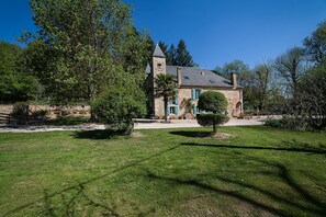 A stone building with a tower, surrounded by well-maintained grass and trees. - Le Moulin De Planiol (Le Vigan)
