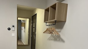 A hotel room with a bed, a wooden wardrobe, a wall-mounted air conditioner, and a hallway leading to a bathroom. - Hôtel Le Ponson (Aubenas)