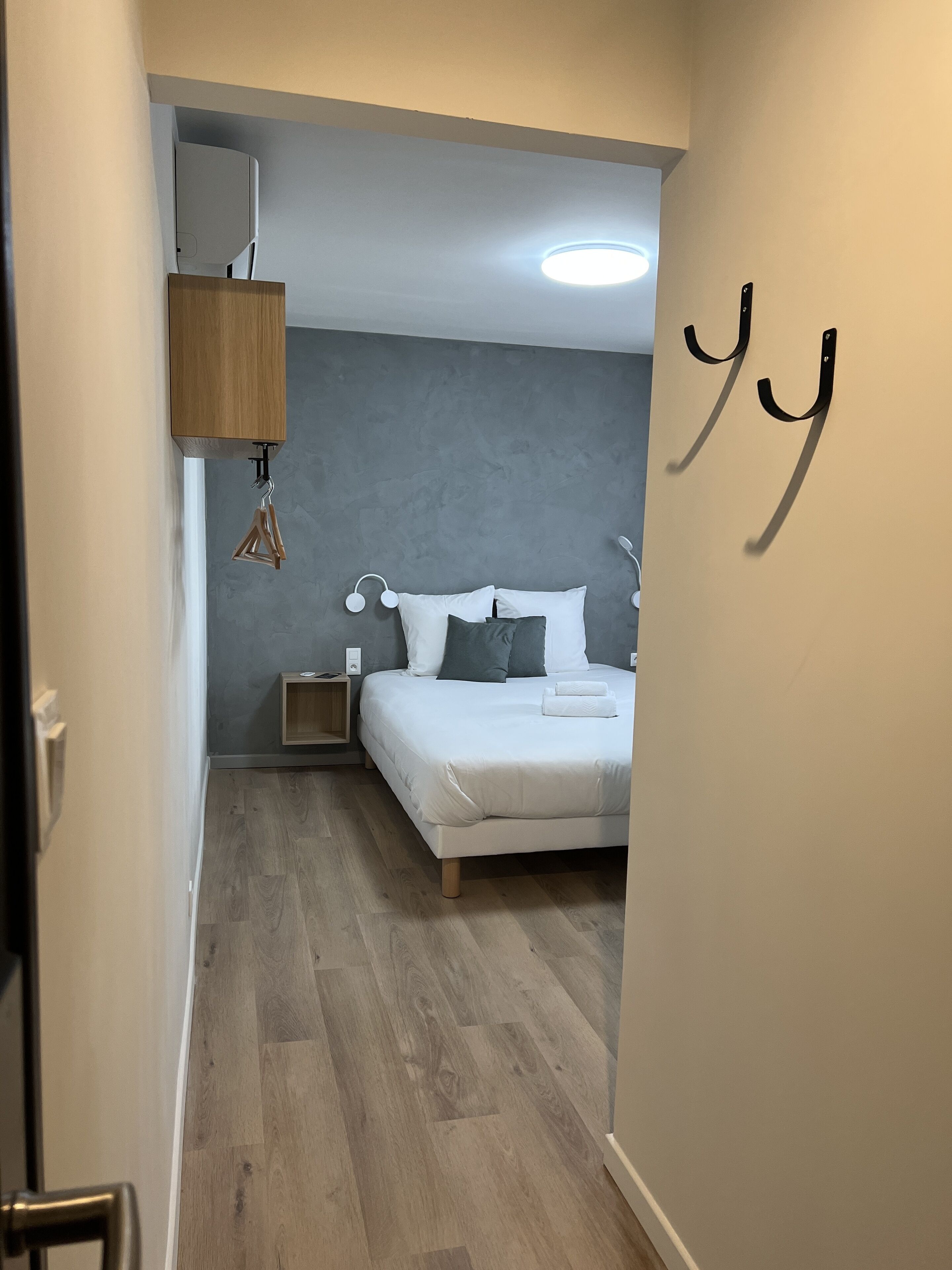 Ett sovrum med en säng, sängbord, en hängande lampa och en väggmonterad handduksställning.