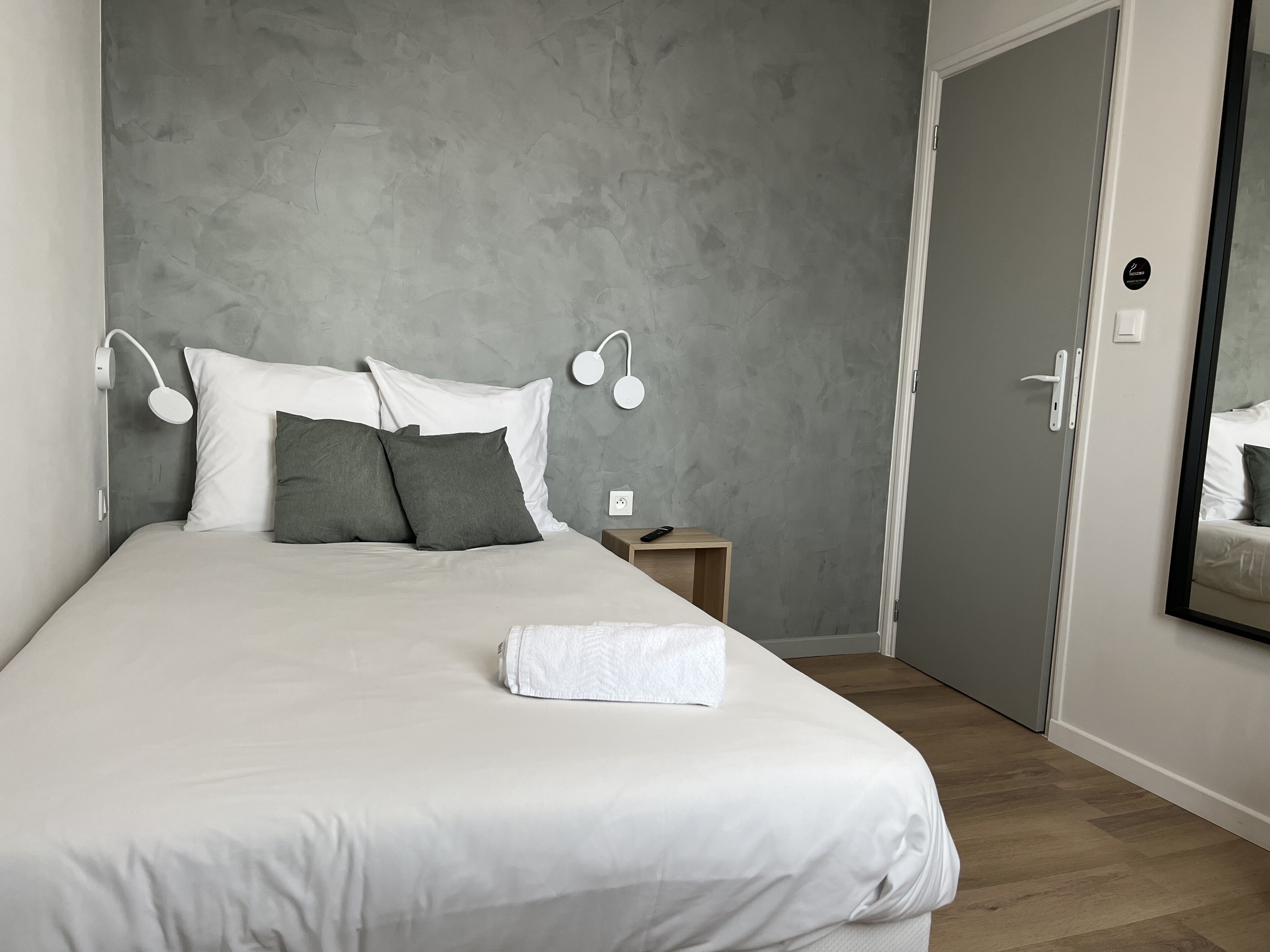 Un dormitorio moderno con una cama grande, paredes grises con textura y suelo de madera.