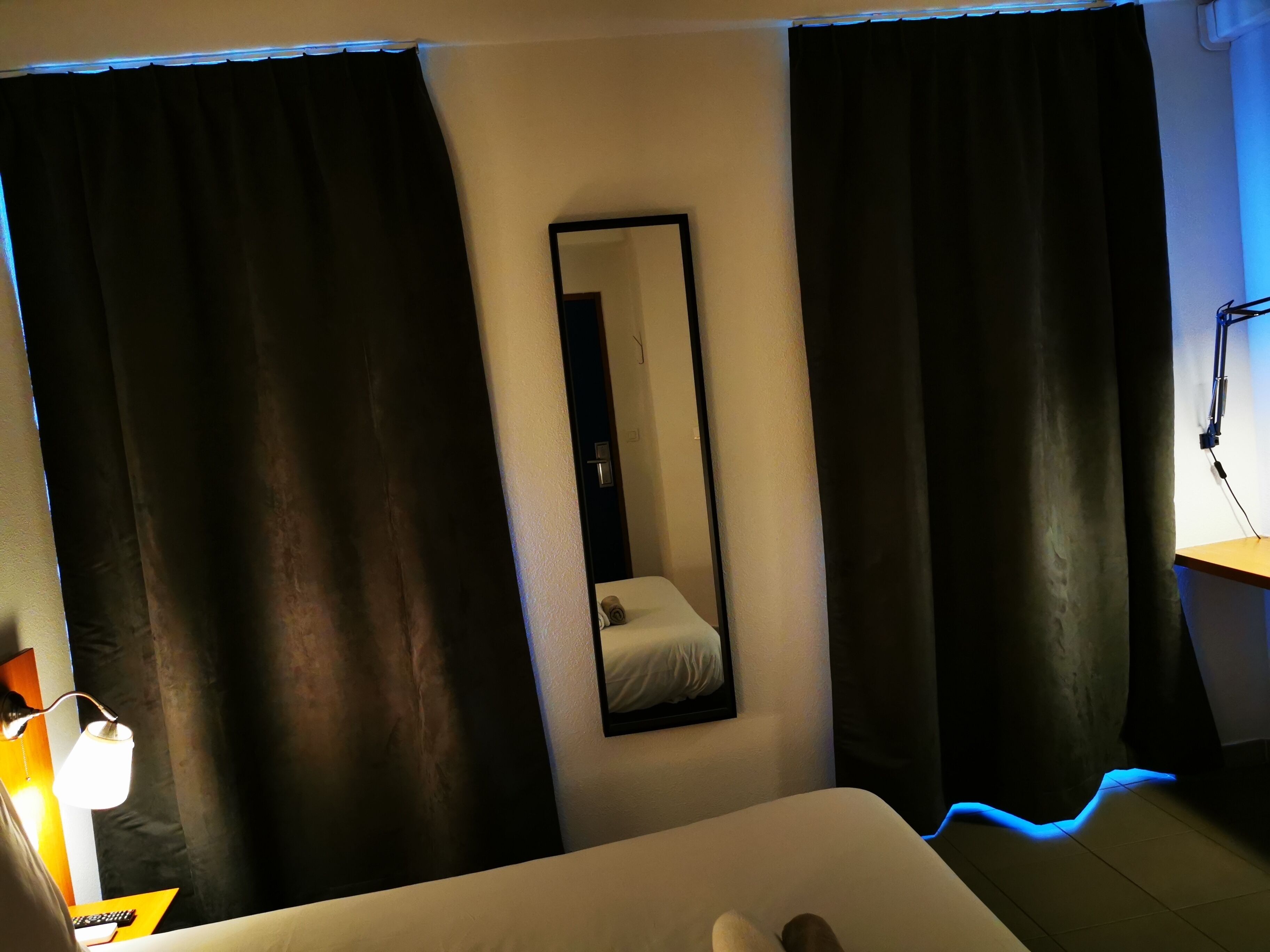 Una habitación de hotel con una cama, un espejo y cortinas negras.