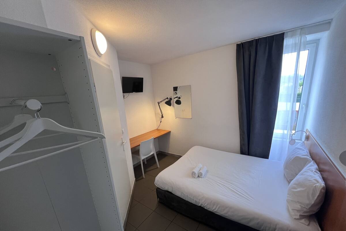 A hotel room with a bed, a desk, a chair, a TV, and a window with curtains.