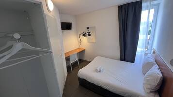 A hotel room with a bed, a desk, a chair, a TV, and a window with curtains.