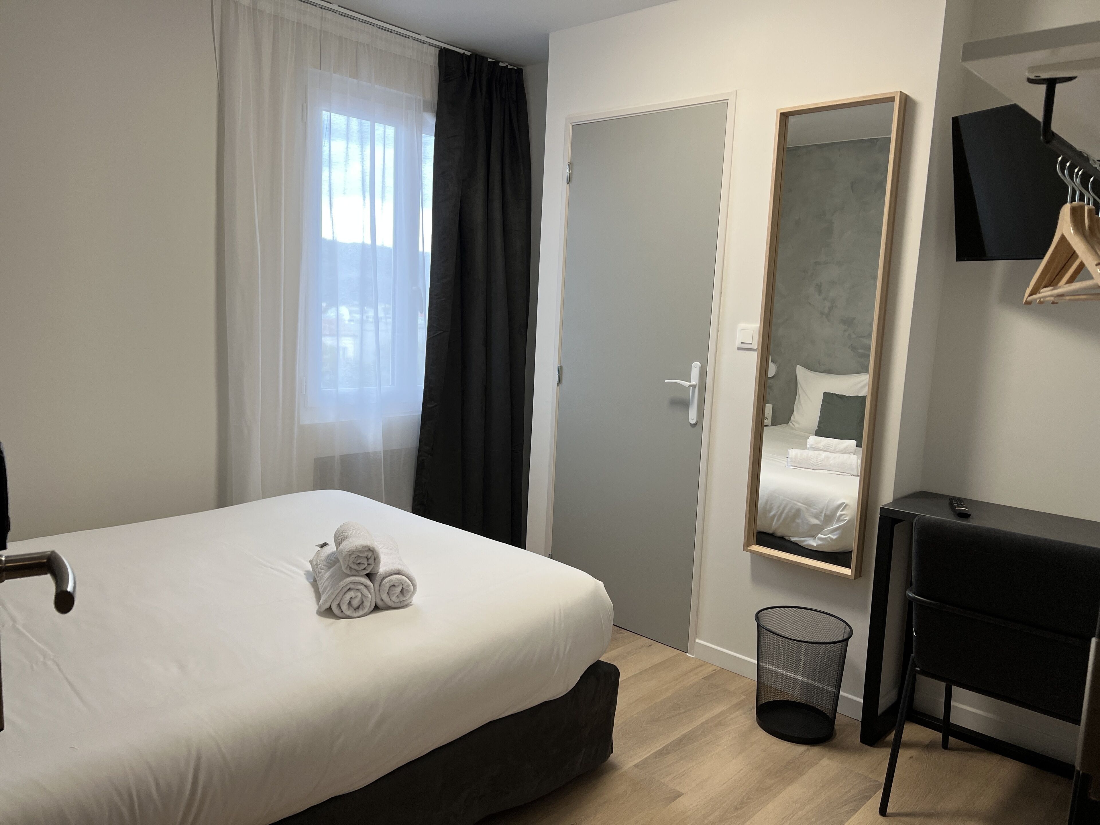 A neatly made bed with rolled towels, a bedside table, a mirror, and a black chair.