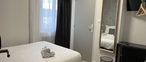 A neatly made bed with rolled towels, a bedside table, a mirror, and a black chair.