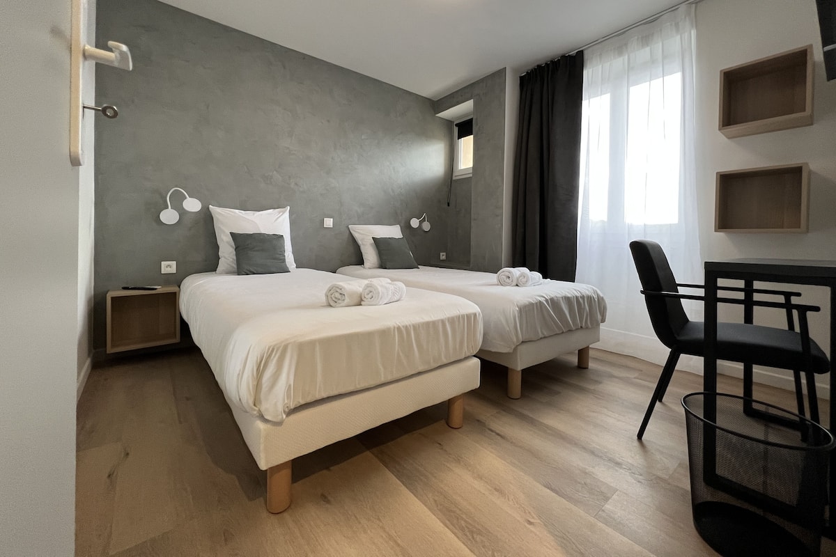 A modern bedroom with two beds, a desk, and a chair.