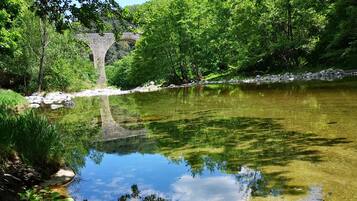 Un río cristalino con un puente de piedra al fondo, rodeado de abundante vegetación.