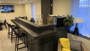 A modern kitchen with a bar area, bar stools, a television, and a potted plant. - Hôtel Le Ponson (Aubenas)