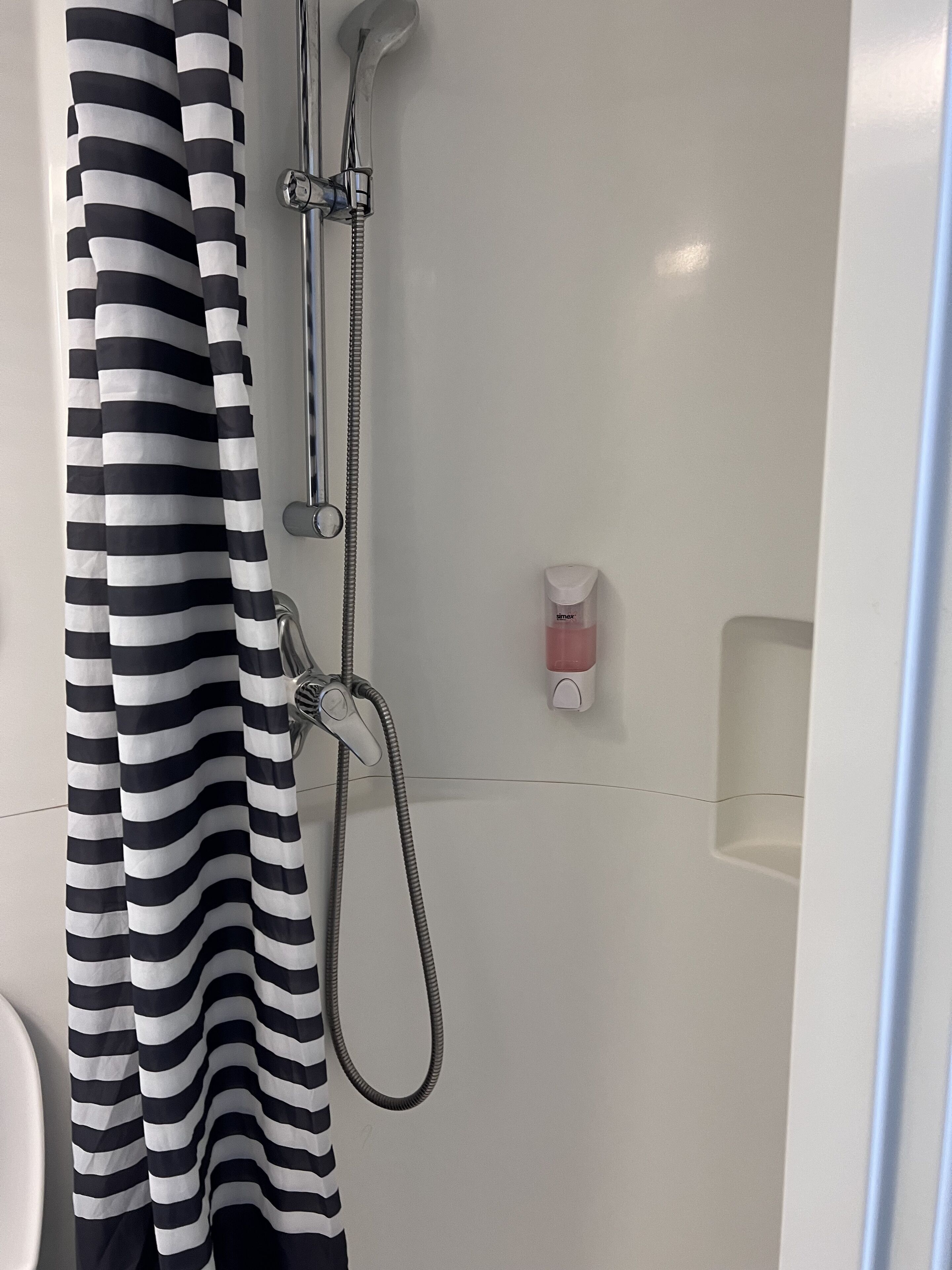 Una ducha con cortina a rayas blancas y negras, un cabezal de ducha manual y un grifo instalado en la pared.