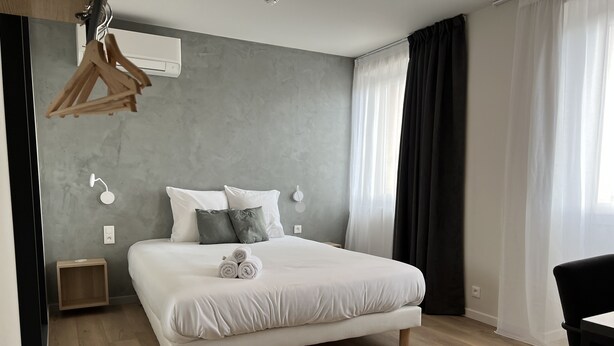 A modern bedroom with a large bed, a bedside table, a hanging light, and a window with curtains. - Hôtel Le Ponson (Aubenas)