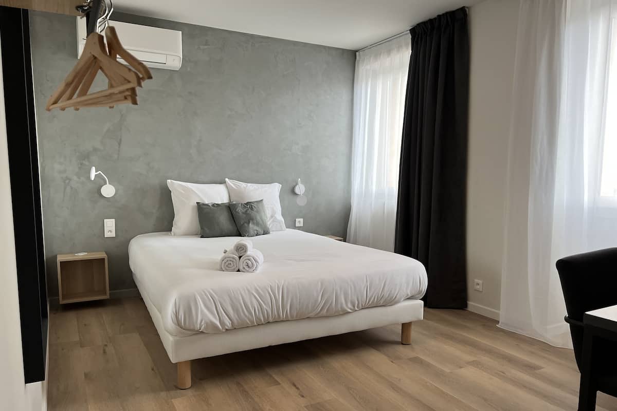 A modern bedroom with a large bed, a bedside table, a hanging light, and a window with curtains.