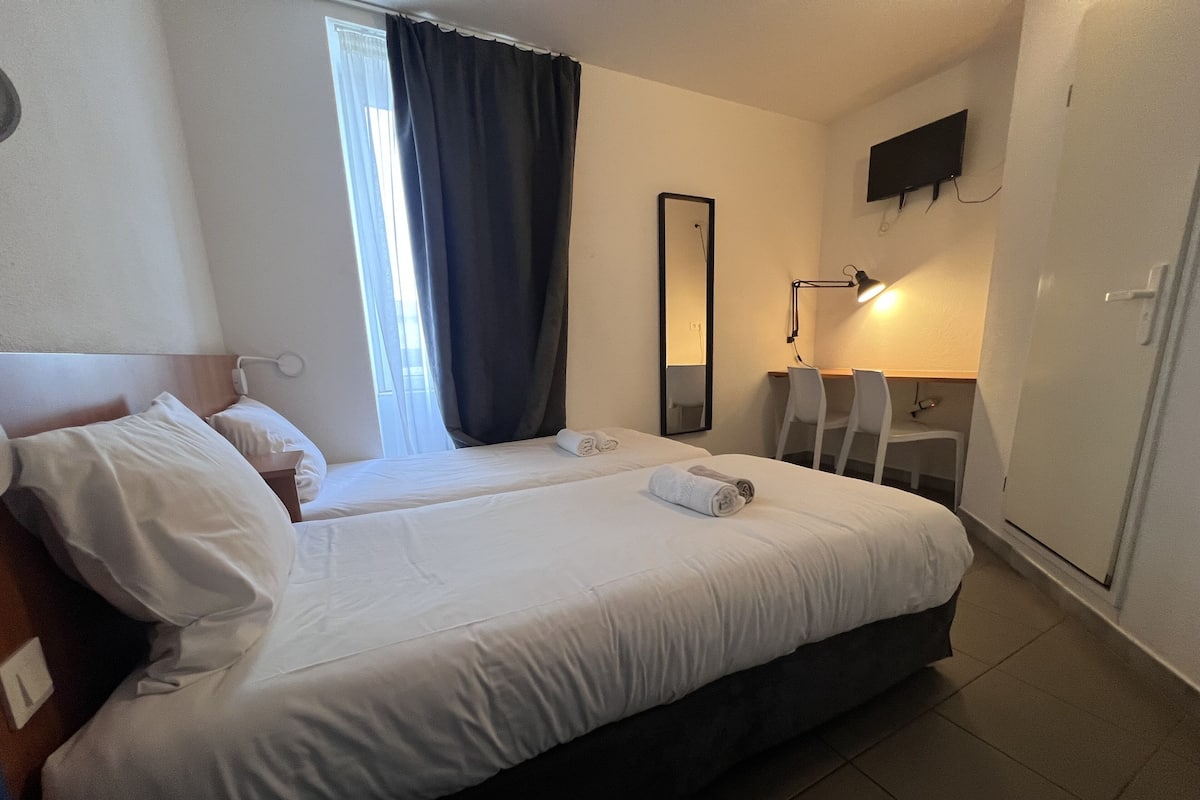 A hotel room with two beds, a desk, a chair, a mirror, and a TV on the wall.