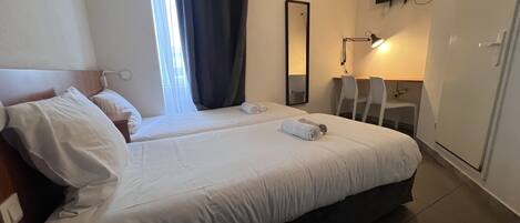 A hotel room with two beds, a desk, a chair, a mirror, and a TV on the wall.