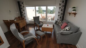 A living room with a wooden dining table, grey sofas, and a coffee table. - Hotell Dalsland (Ed)