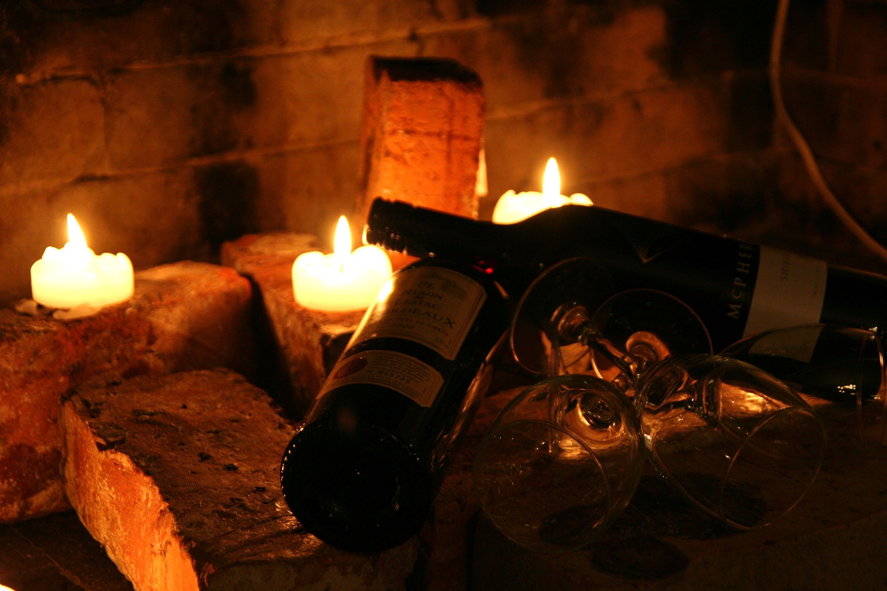 A bottle of wine, a glass, and lit candles on a brick surface.