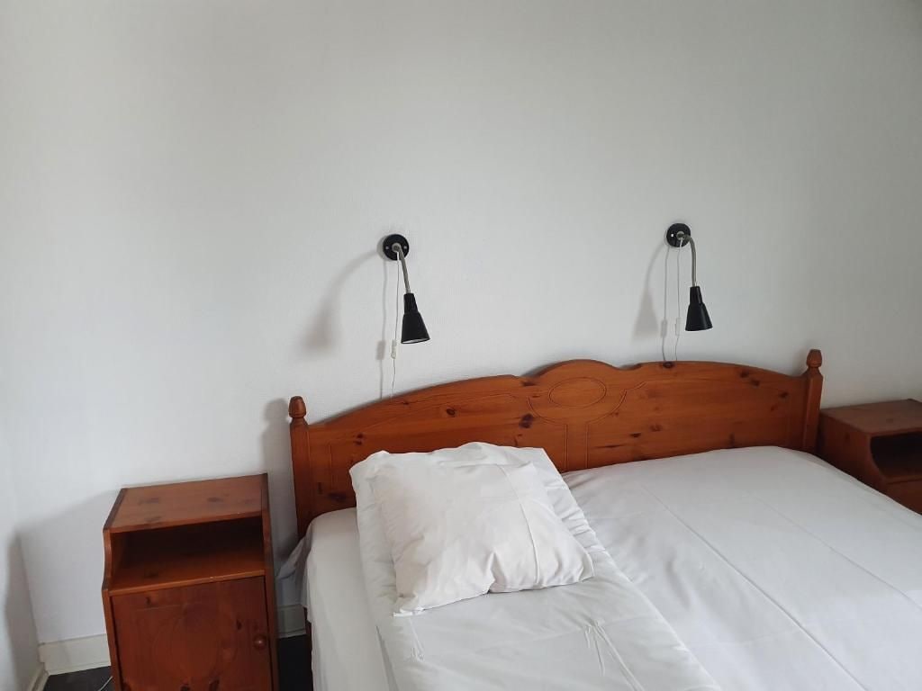 A single bed with a wooden headboard, two bedside tables, and two wall-mounted lamps.