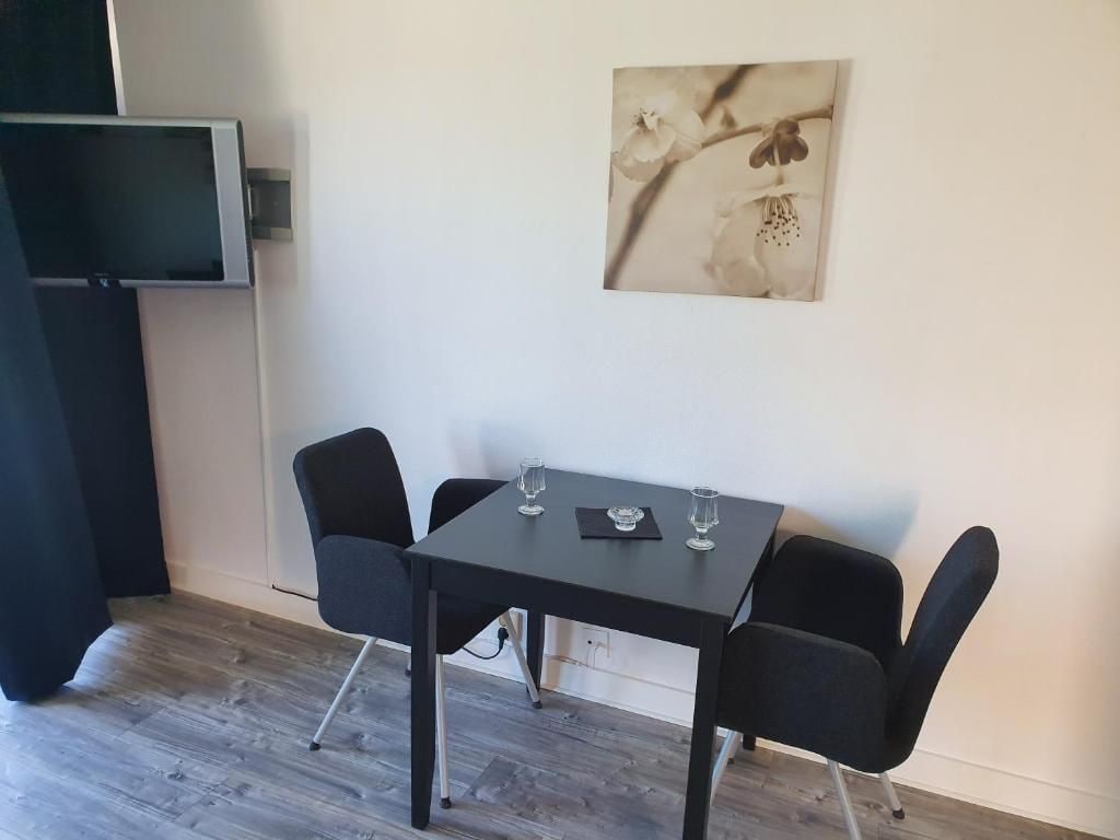 Una habitación con una mesa negra y cuatro sillas, un televisor de pantalla plana montado en la pared, y un cuadro con flores.