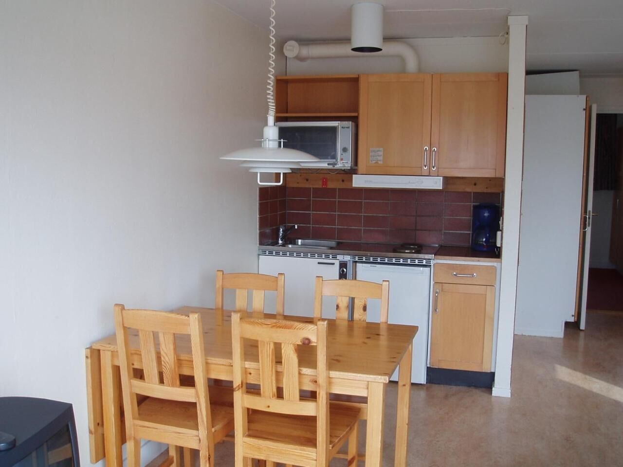 Cocina pequeña con armarios de madera, microondas y estufa. Hay una mesa de comedor con sillas.