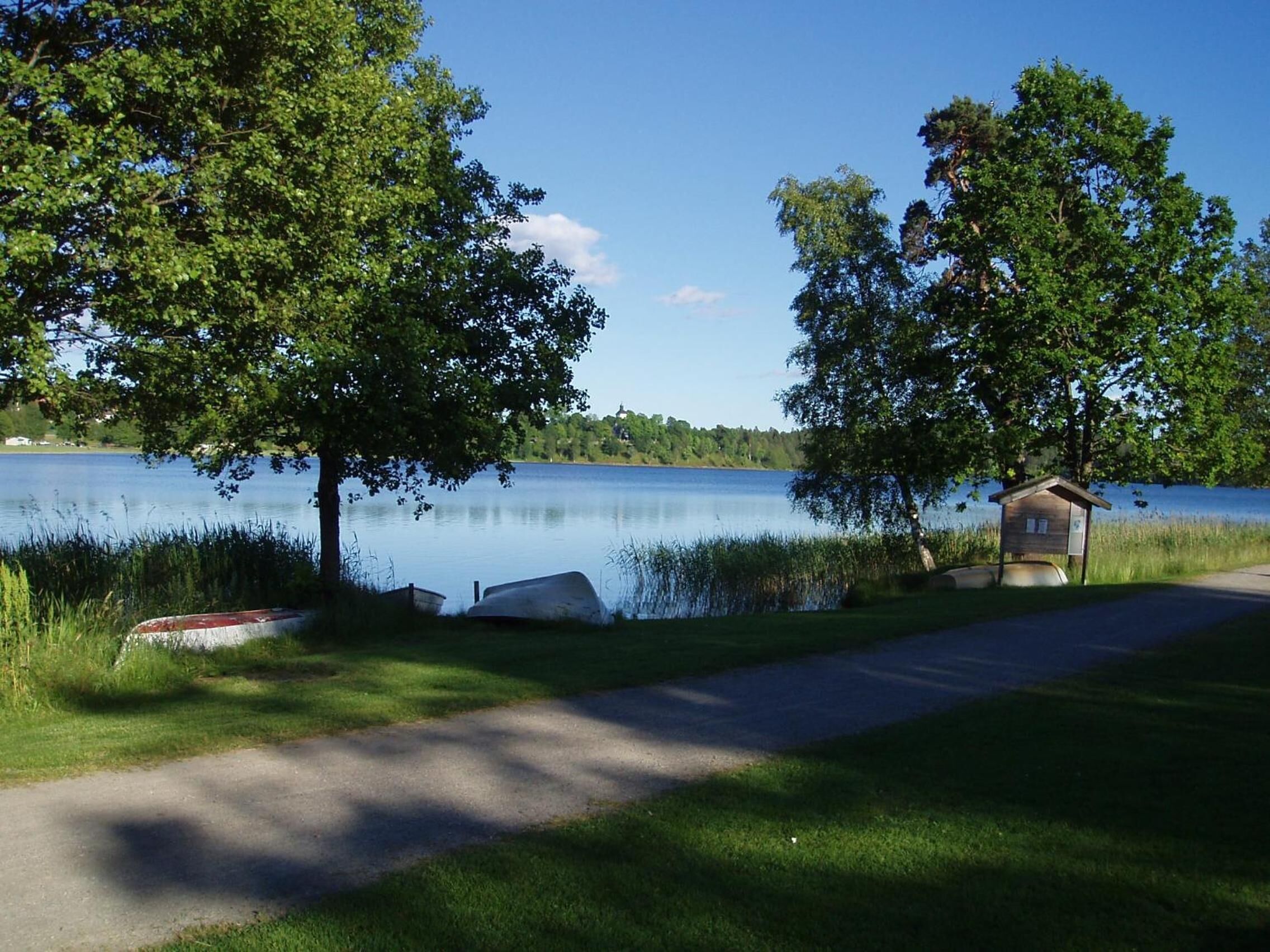 A lakeside path with boats, a small wooden structure, and trees.