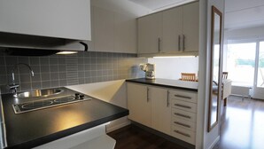 A modern kitchen with a black countertop, stainless steel sink, and white cabinets. - Hotell Dalsland (Ed)