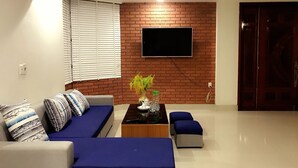 A modern living room with a brick accent wall, a flat-screen TV mounted above a wooden coffee table, and a sofa with blue cushions. - Sky Halong Hotel (Bai Chay)